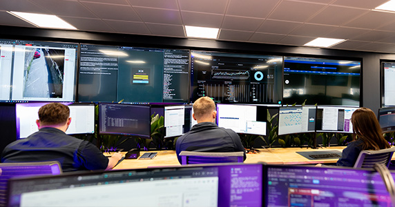 Three operative working at their computers in front of a wall of screens