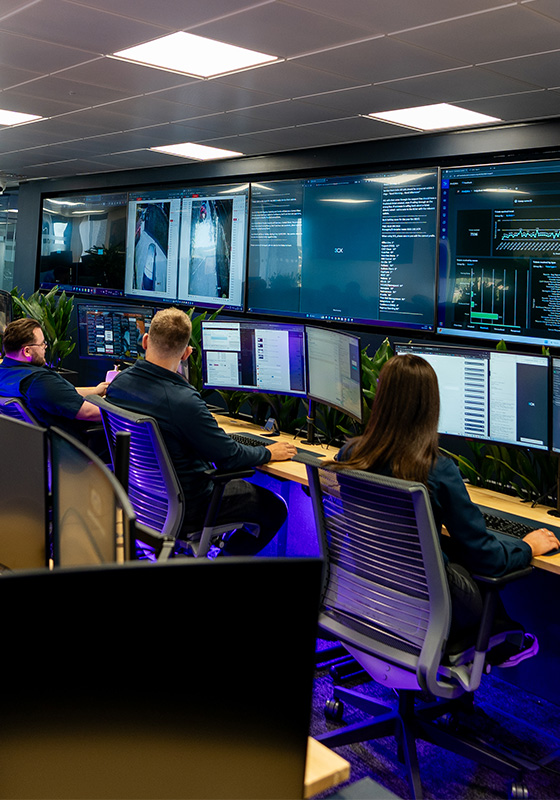 Three operatives working in front of a wall of screens showing stats