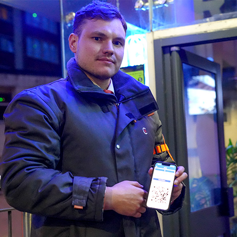 A security guard stood outside a nightclub showing the camera his phone with the c247 app loaded